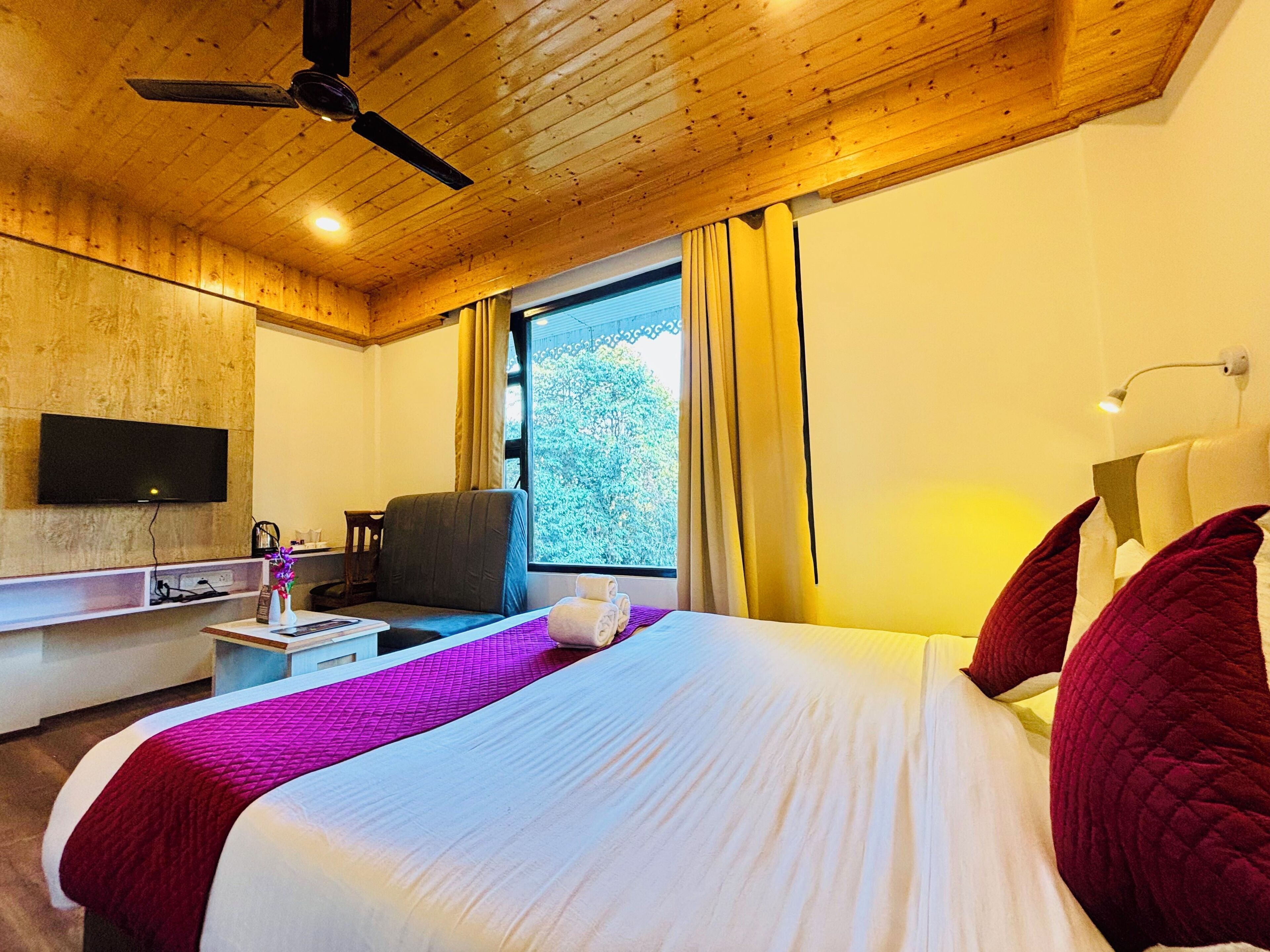 Habitación de hotel con cama, escritorio, silla, televisor y ventana con cortinas.