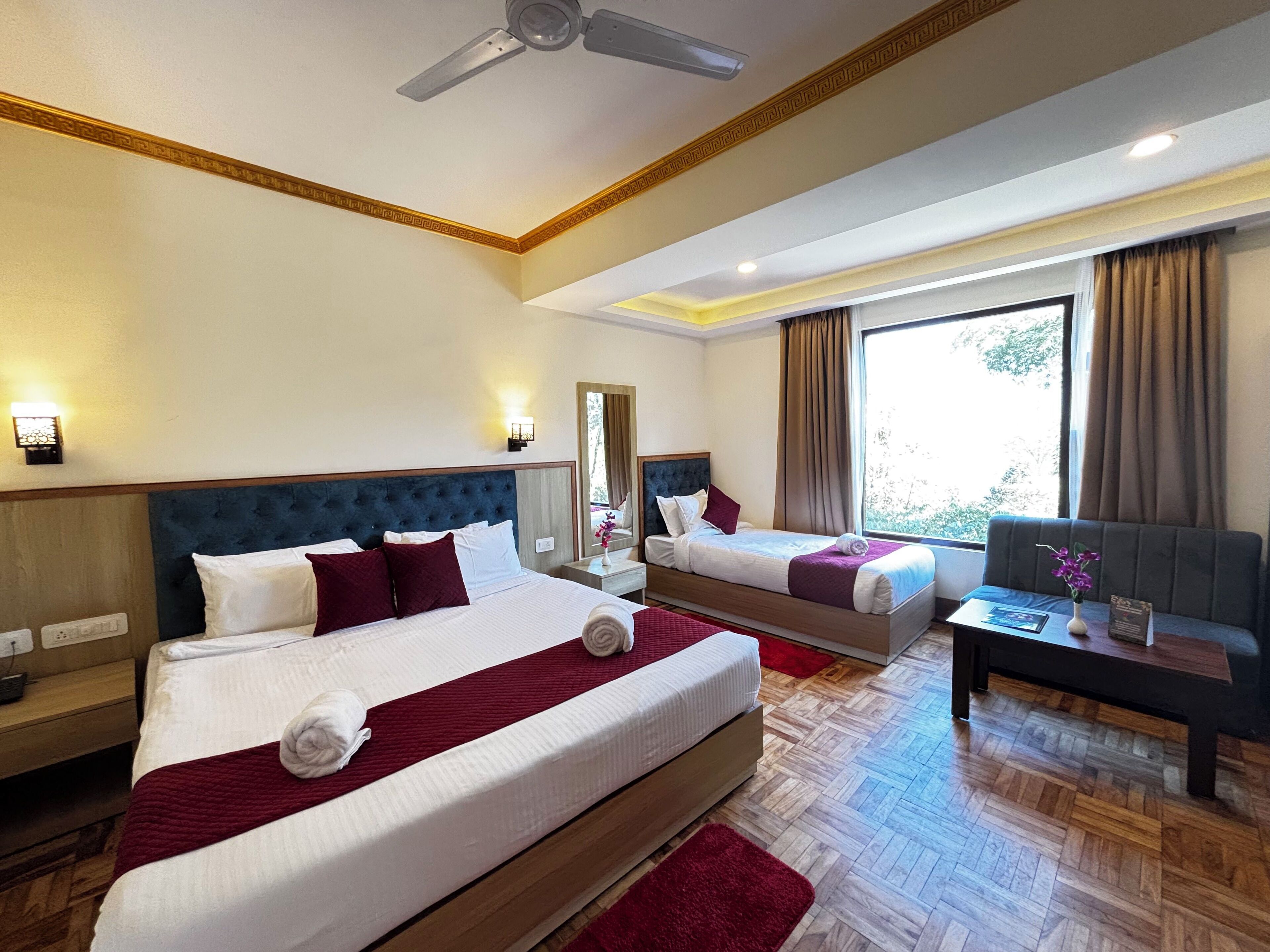 A hotel room with two beds, a sofa, a small table, and a ceiling fan.