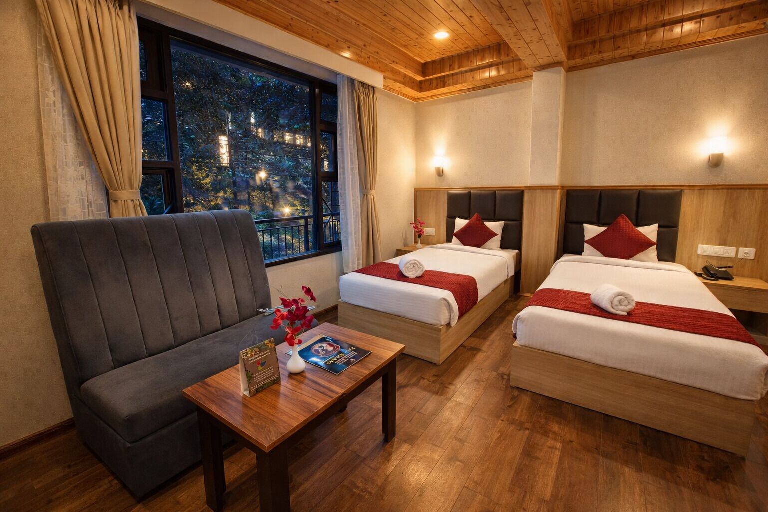 A hotel room with two beds, a sofa, a wooden table, and a window with a night view.