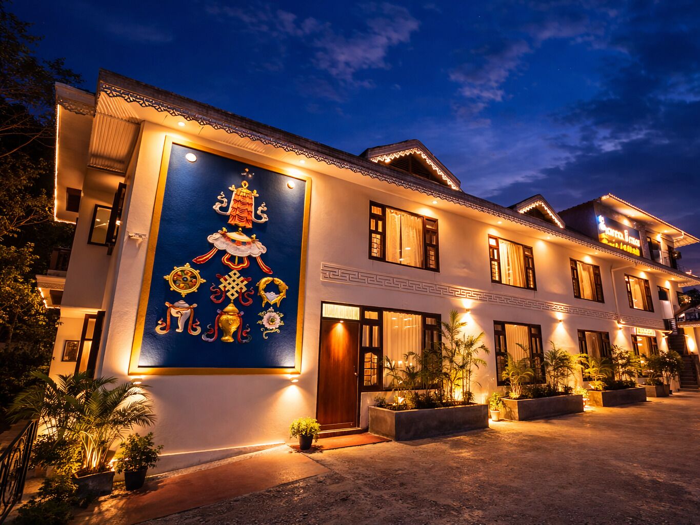 A multi-story hotel with a traditional architectural design, featuring a large decorative mural on the facade, multiple windows, and a well-lit entrance area.