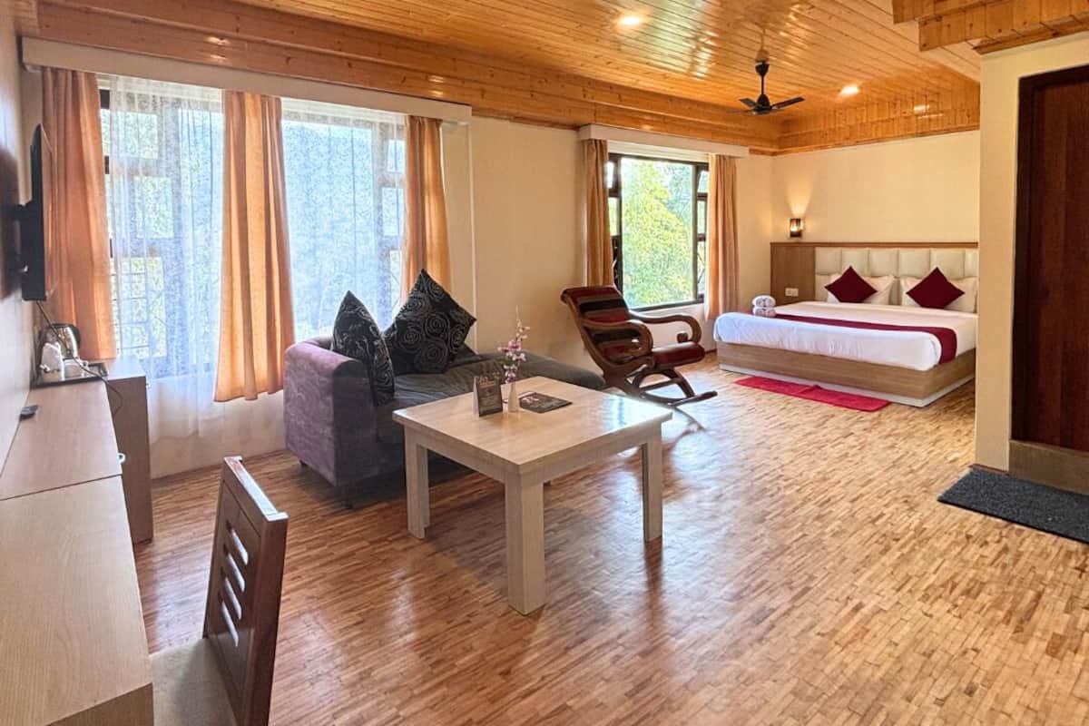 A spacious room with a wooden ceiling, a bed with red bedding, a sofa, a rocking chair, and a dining area.