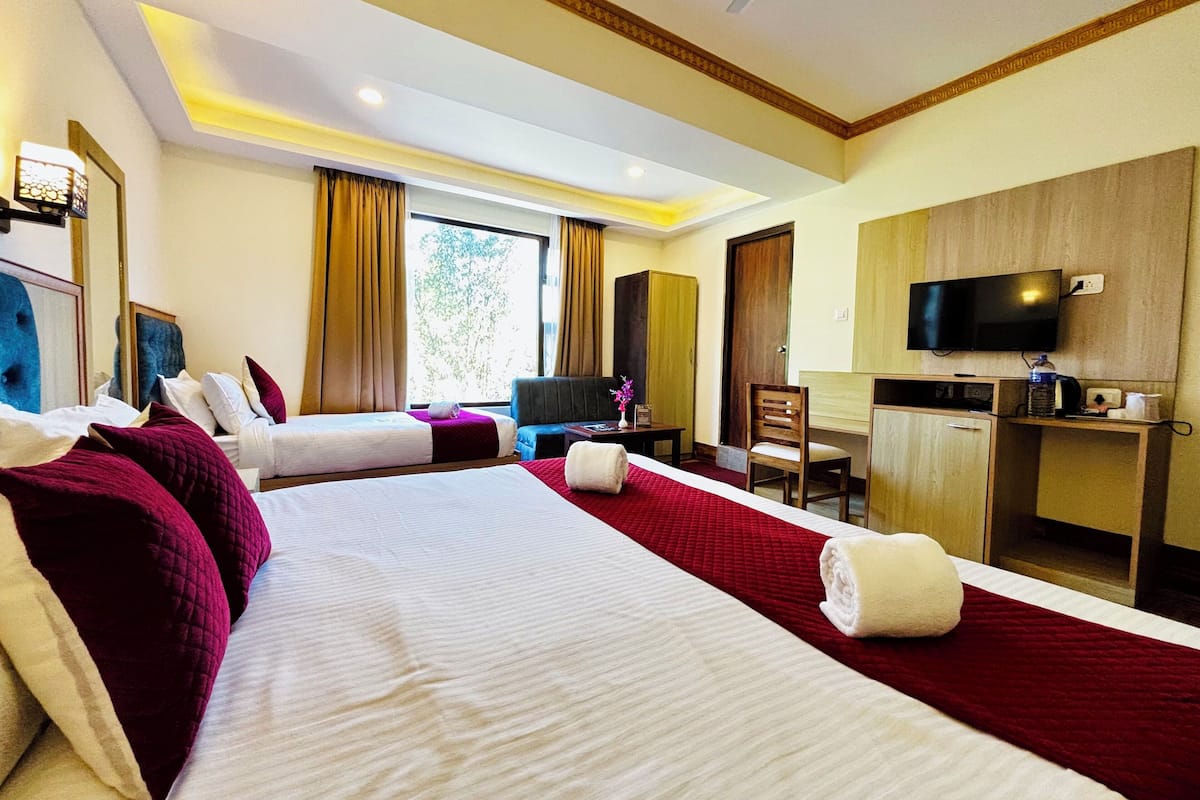 A hotel room with two beds, a desk, a television, and a window with curtains.