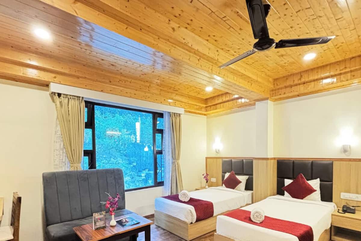 A hotel room with two beds, a sofa, a small table, and a ceiling fan.