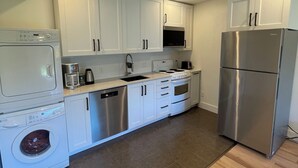 A modern kitchen with white cabinets, stainless steel appliances, and a wooden floor.