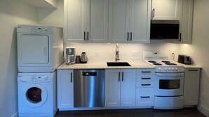 A compact kitchen with white cabinets, a dishwasher, a coffee maker, a microwave, and an oven.