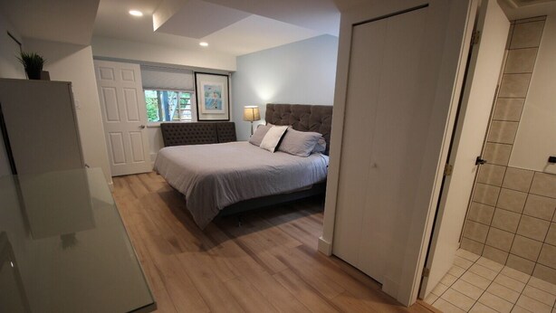 A bedroom with a bed, a bedside table, a lamp, and a window.