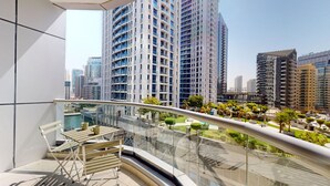 A modern high-rise building with a glass balcony overlooking a landscaped area with trees and a pool. - The Point Tower - Vibrant One Bed in Marina (Dubai Marina)