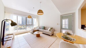 A modern living room with a sofa, coffee table, and dining table set for two. Large windows provide a view of the cityscape. - The Point Tower - Vibrant One Bed in Marina (Dubai Marina)
