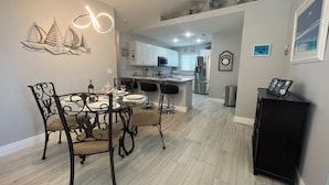 A modern kitchen with white cabinets, a stainless steel refrigerator, and a dining area with a glass table and metal chairs. - The White Egret, Private heated Pool, Fresh Water Canal, Beach, Fishing, WIFI (Cape Coral)