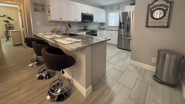 A modern kitchen with white cabinets, stainless steel appliances, and a central island with bar stools. - The White Egret, Private heated Pool, Fresh Water Canal, Beach, Fishing, WIFI (Cape Coral)
