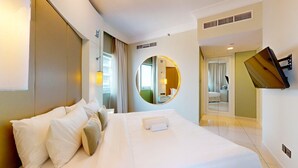 Habitación de hotel con una cama grande, un espejo redondo, un televisor montado en la pared y un baño visible a través de una puerta abierta.