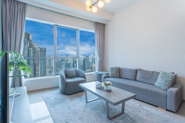 A modern living room with a sofa, armchair, and coffee table, large windows with a city view, and a potted plant.