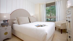 Un dormitorio ordenado con cama, mesita de noche, lámpara y una silla.