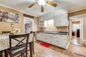 A kitchen with white cabinets, a wooden ceiling fan, and a dining area with a table and chairs.