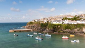 A coastal town with boats docked near a rocky shore, houses on a hillside, and a clear blue sky. - Port Gaverne Hotel (Port Isaac)