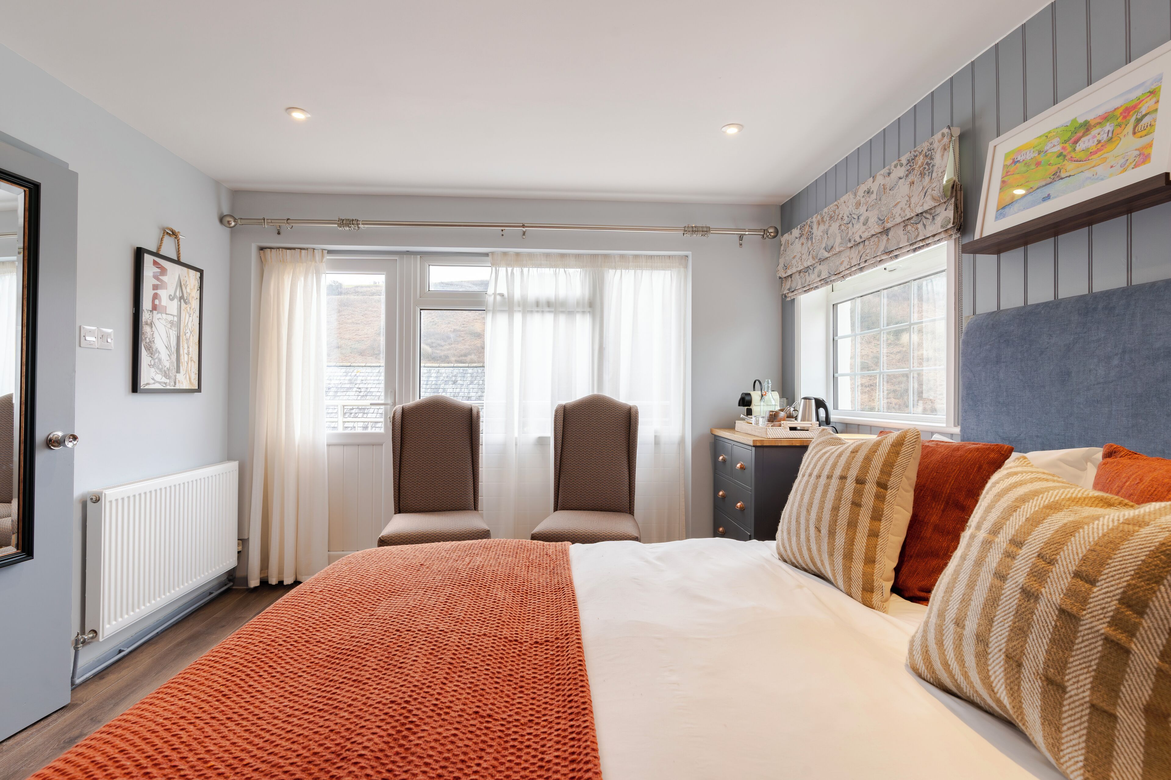 A bedroom with a large bed, two chairs, a dresser, and a window with curtains.