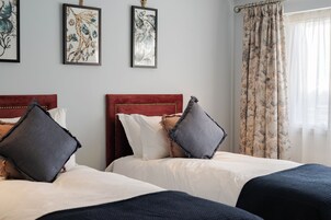 Dos camas con cabeceras rojas, ropa de cama blanca y almohadones decorativos.