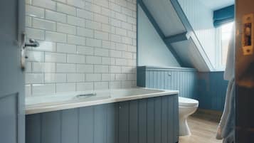 A bathroom with white tiled walls, a blue vanity, a white toilet, and a wooden floor.