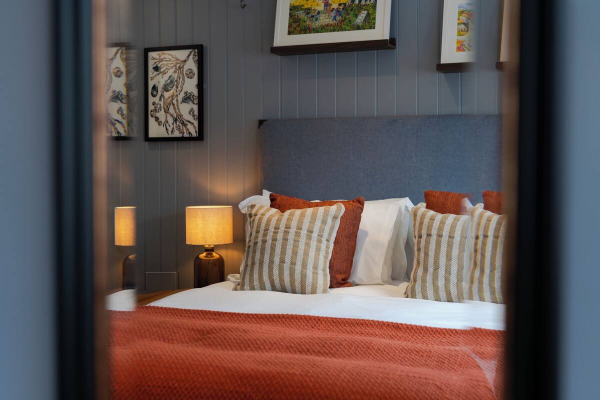 A neatly made bed with striped pillows and a red blanket, a bedside lamp, and framed artwork on the wall.