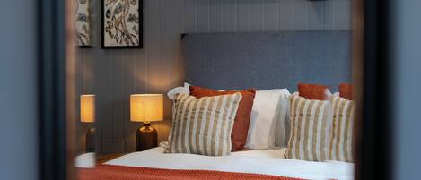 A neatly made bed with striped pillows and a red blanket, a bedside lamp, and framed artwork on the wall.