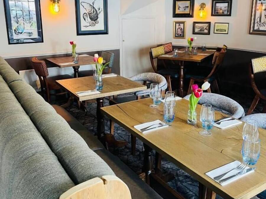A cozy restaurant with wooden tables and chairs, framed artwork on the walls, and a stone floor.