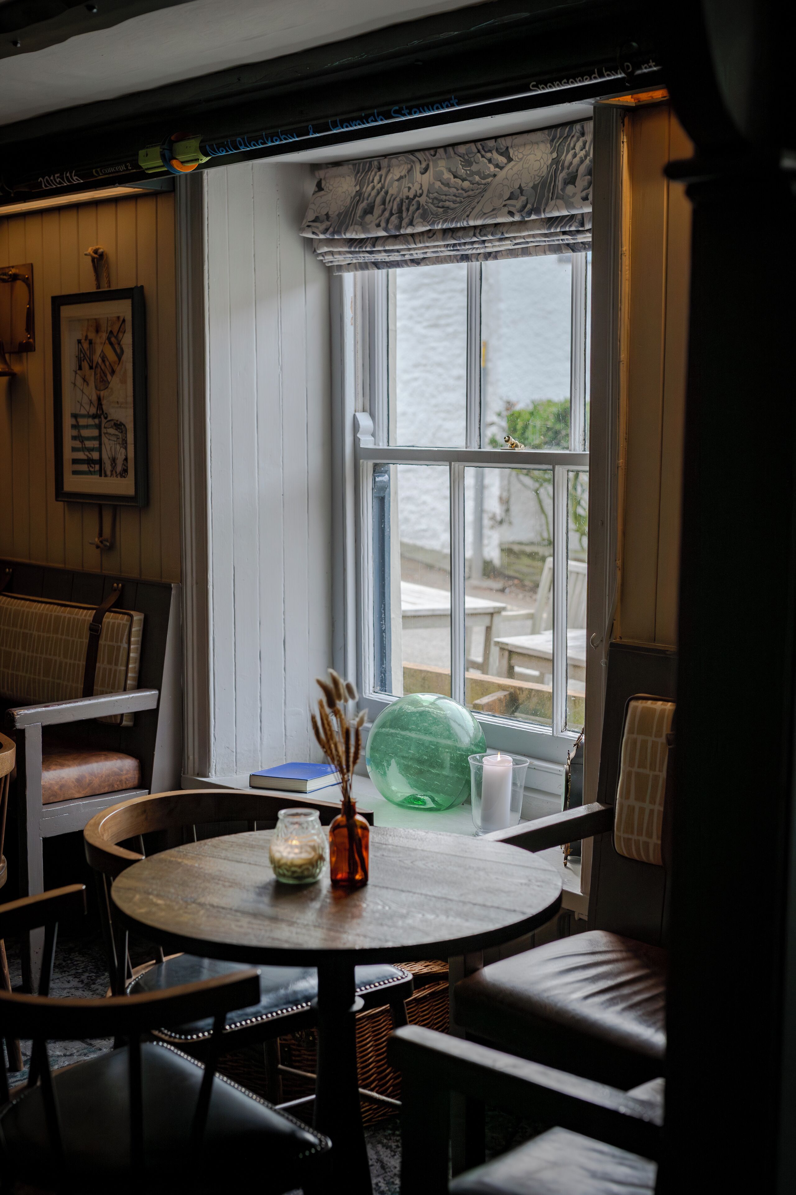 A cozy room with a round table, chairs, a window with a view, and a framed picture on the wall.