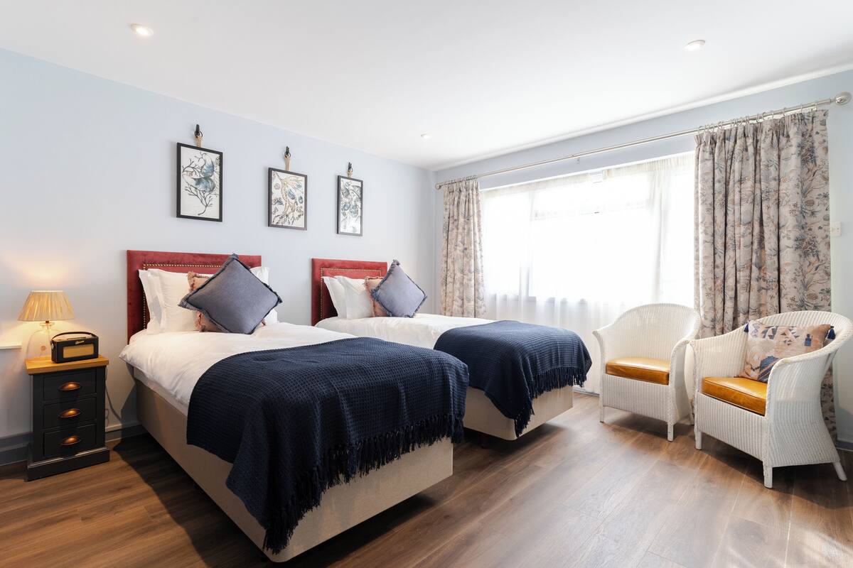 A hotel room with two beds, a chair, a nightstand, and framed artwork on the wall.