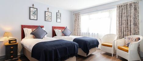 A hotel room with two beds, a chair, a nightstand, and framed artwork on the wall.