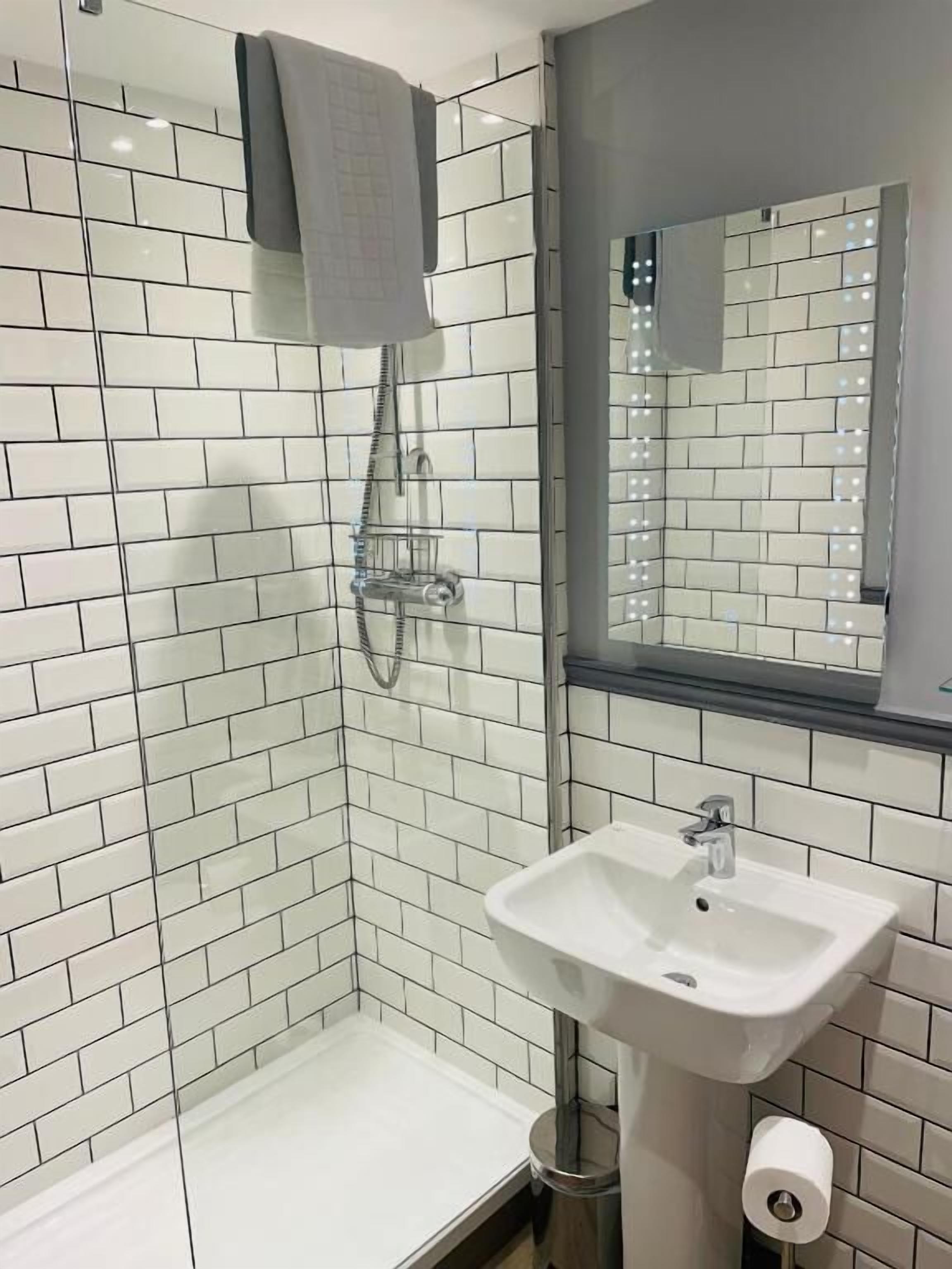 Een moderne badkamer met witte metrotegels, een glazen douchecabine, een wastafel met spiegel en een handdoekrek.