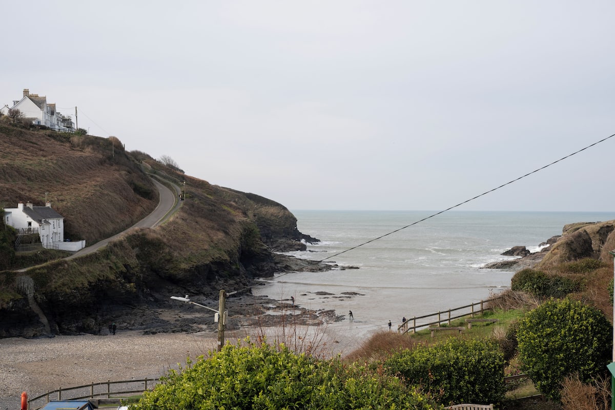 A coastal road with a white building on a hill, a rocky beach, and the sea.
