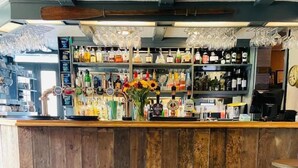 A bar area with wooden counter, shelves of bottles, and hanging glasses. - Port Gaverne Hotel (Port Isaac)