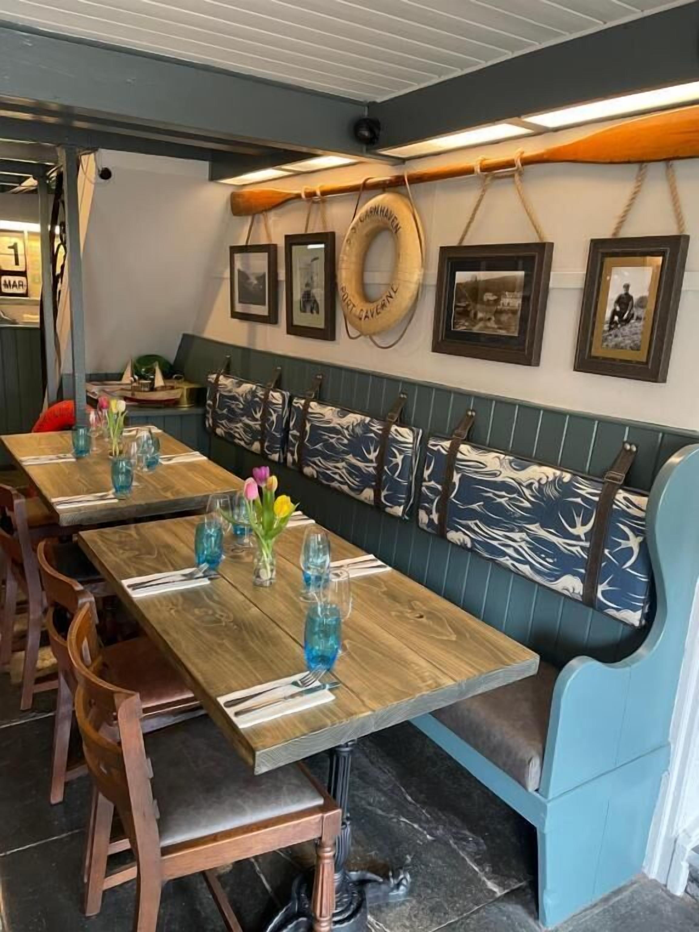 A restaurant interior with wooden tables, blue upholstered benches, and framed pictures on the wall.