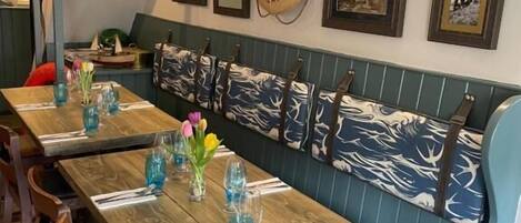 A restaurant interior with wooden tables, blue upholstered benches, and framed pictures on the wall.