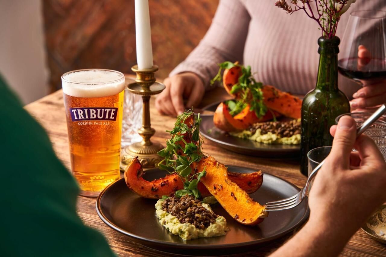 A dining table with a glass of beer, a candle, and a plate of food.