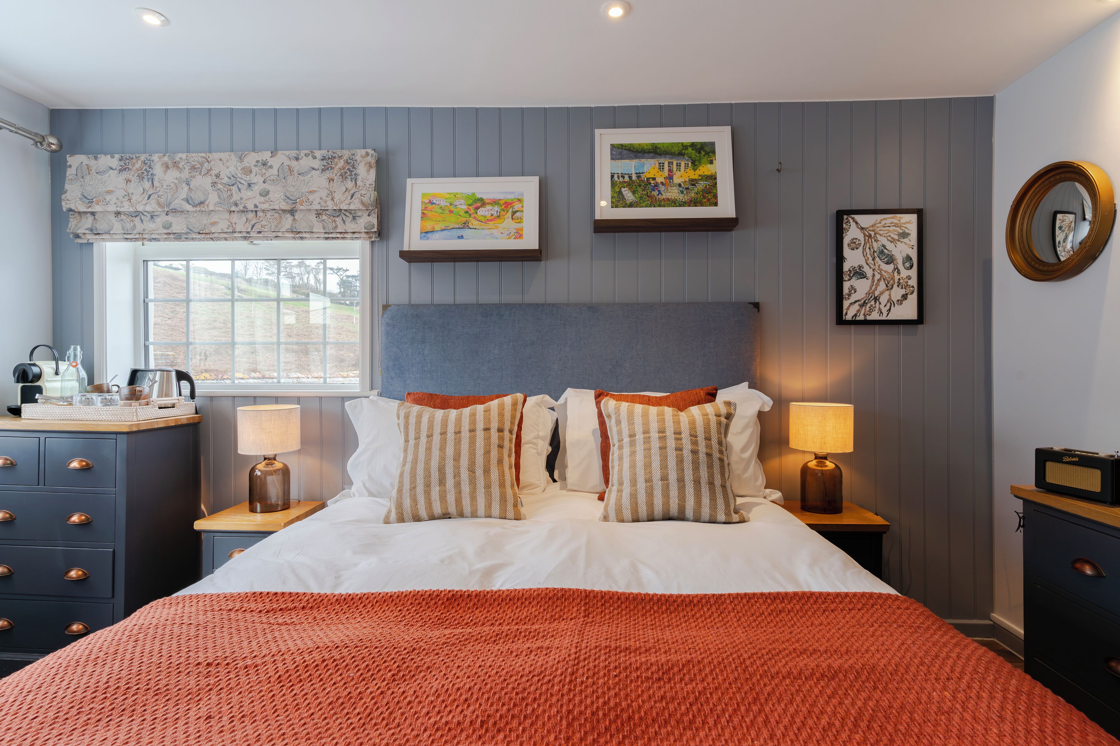 A neatly arranged bedroom with a large bed, two bedside tables, a dresser, and a window with curtains.