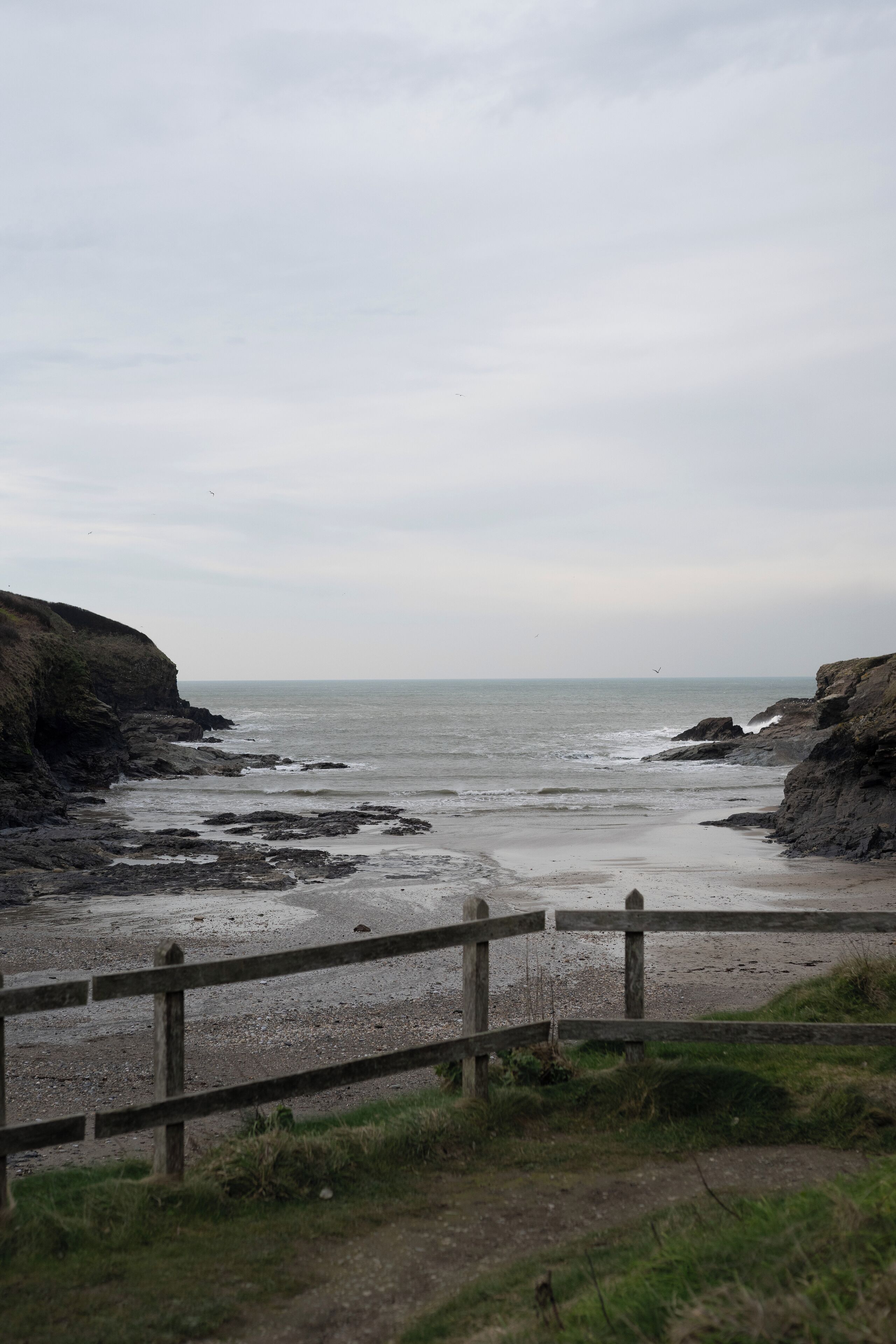 A coastal view with a wooden fence, rocky cliffs, and the sea.
