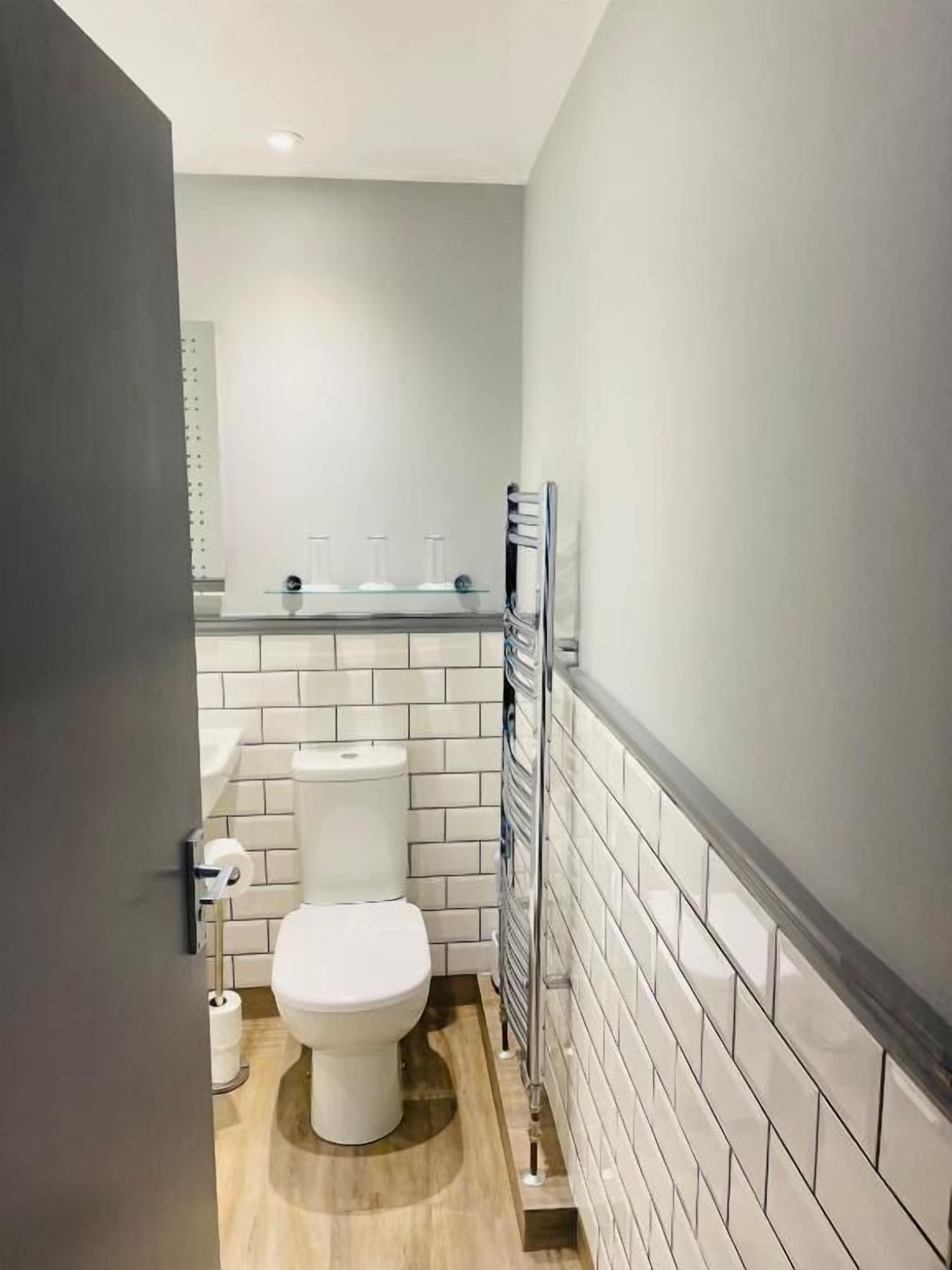 A compact bathroom with a white toilet, a glass shelf with toiletries, and a towel rack.