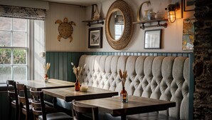 A restaurant interior with a tufted bench seating, wooden tables, and chairs. - Port Gaverne Hotel (Port Isaac)