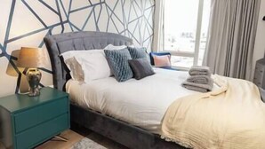 Un dormitorio con cama, mesita de noche, lámpara y vistas al exterior.