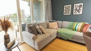 Una sala de estar con un sofá gris, una manta verde a rayas y dos cuadros en la pared.