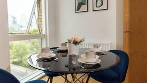 Un comedor con una mesa redonda, sillas azules y un jarrón con flores. Hay dos cuadros en la pared.