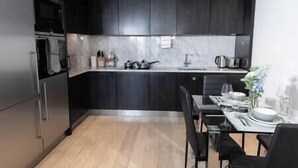 Una cocina moderna con armarios oscuros, encimera de mármol y comedor con mesa y sillas.