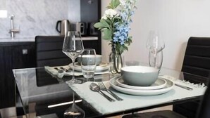 Una mesa de comedor dispuesta con platos, tazones, vasos y cubiertos, junto con un jarrón de flores.