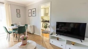 A modern living room with a dining area, a flat-screen TV, and a view into the kitchen.