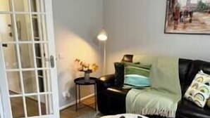 A living room with a black leather sofa, a round coffee table, a white lamp, and a framed picture on the wall.