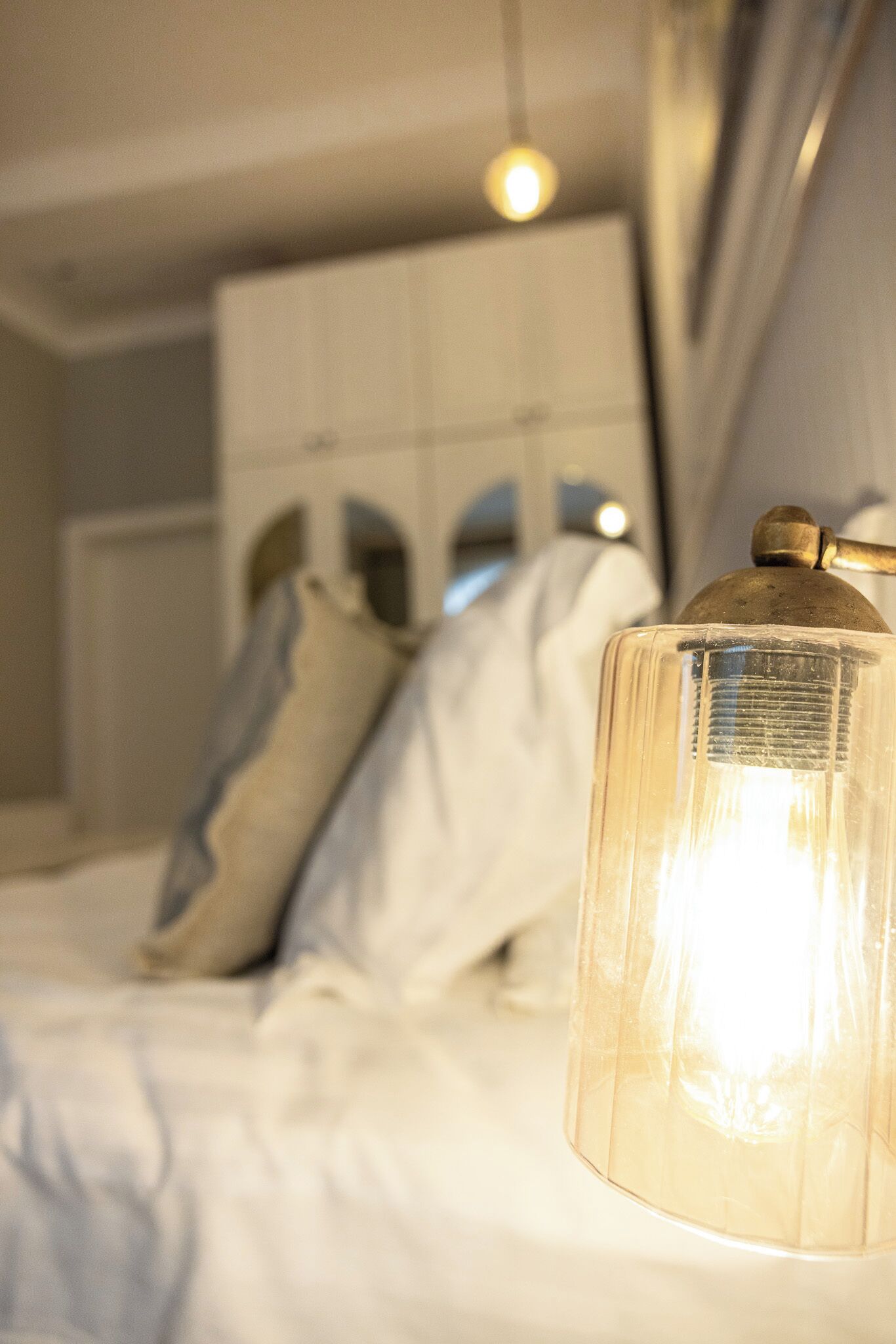 Una cama con ropa blanca y una lámpara de cristal con base de bronce.