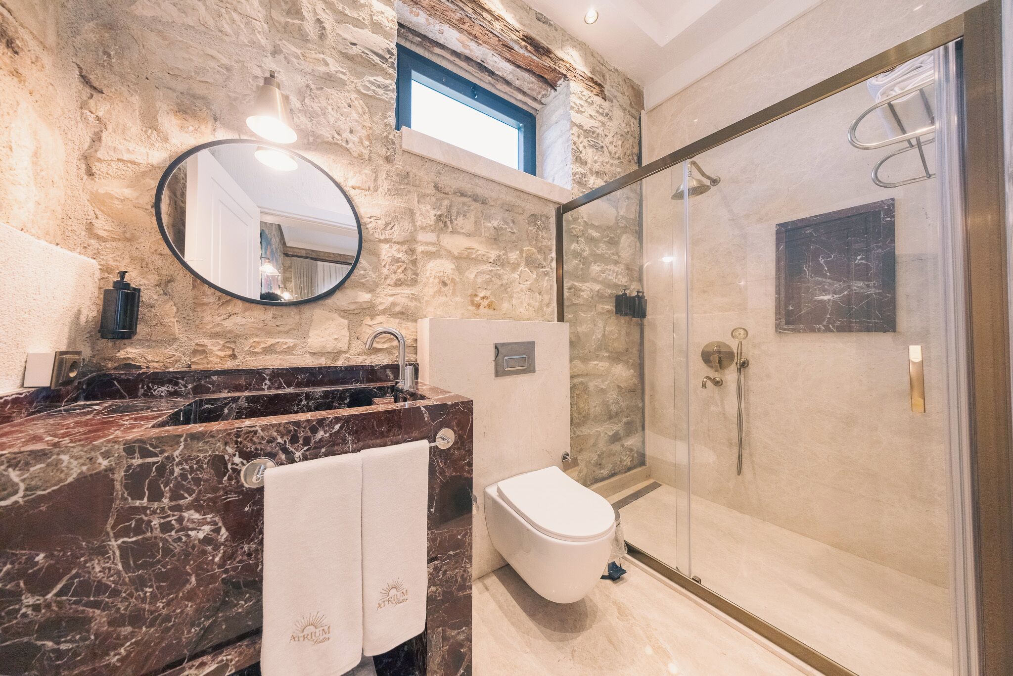 A bathroom with a stone wall, a marble sink, a toilet, and a glass-enclosed shower.