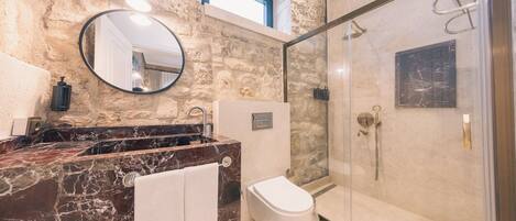 A bathroom with a stone wall, a marble sink, a toilet, and a glass-enclosed shower.