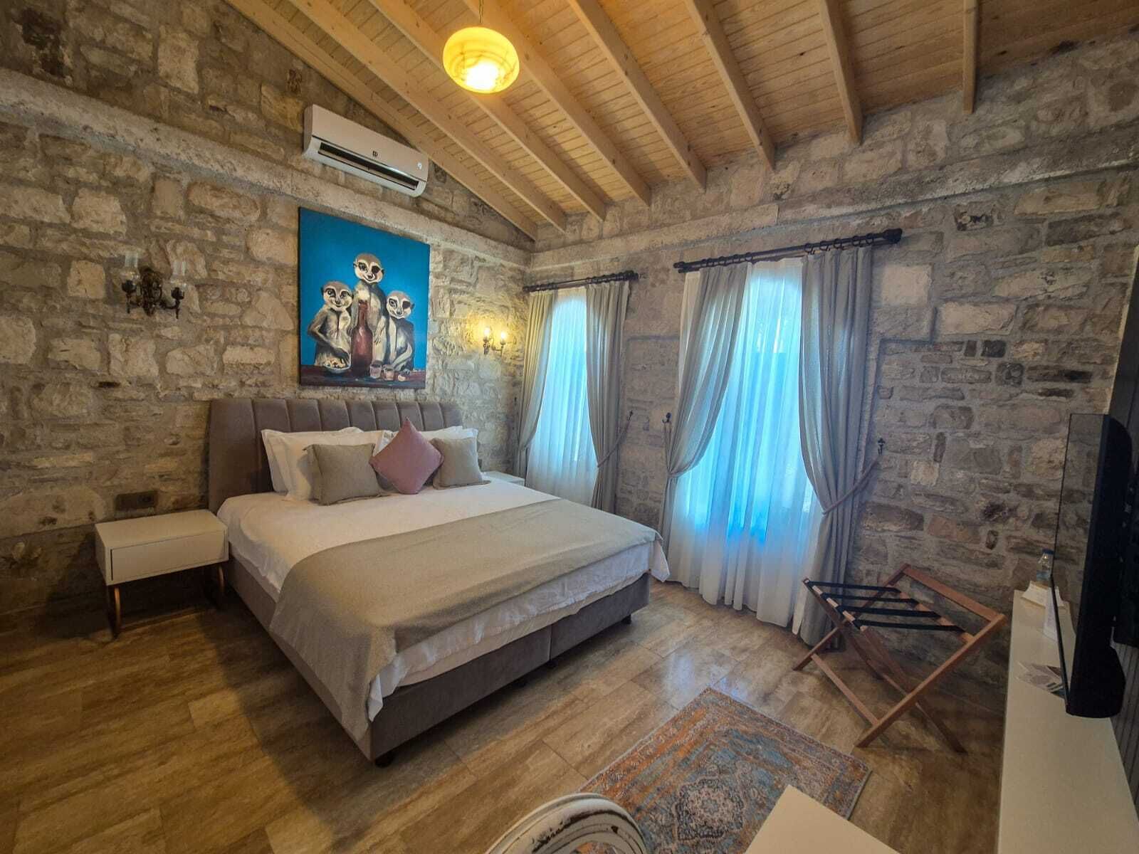 A bedroom with a stone wall, a bed, a nightstand, a painting, and a wooden ceiling.