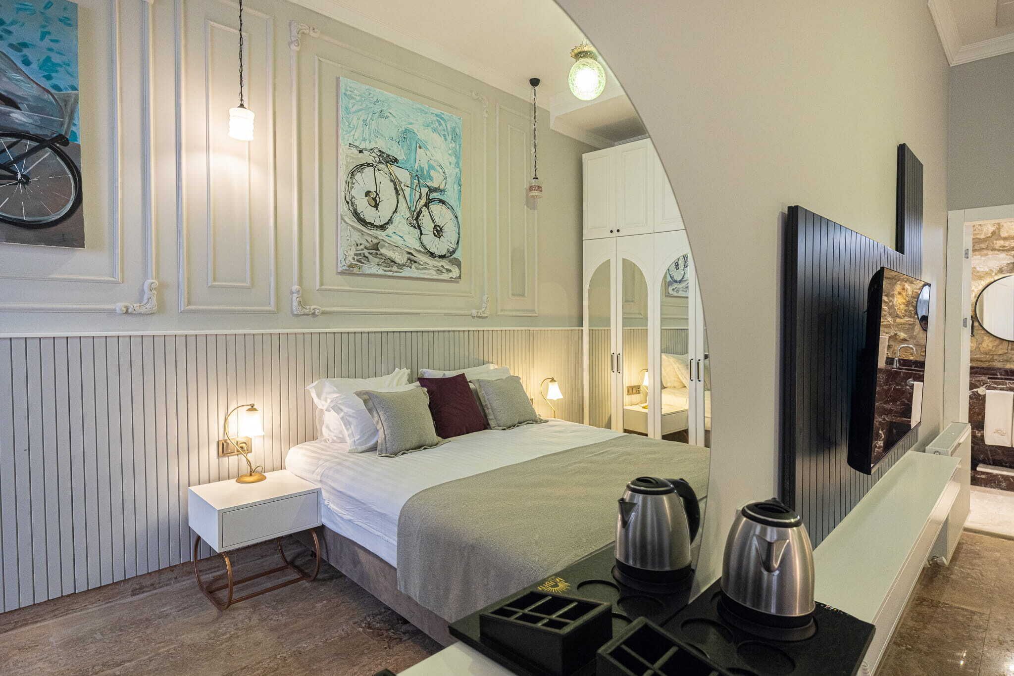 Una habitación de hotel con cama, mesita de noche, cafetera y una obra de arte en la pared.